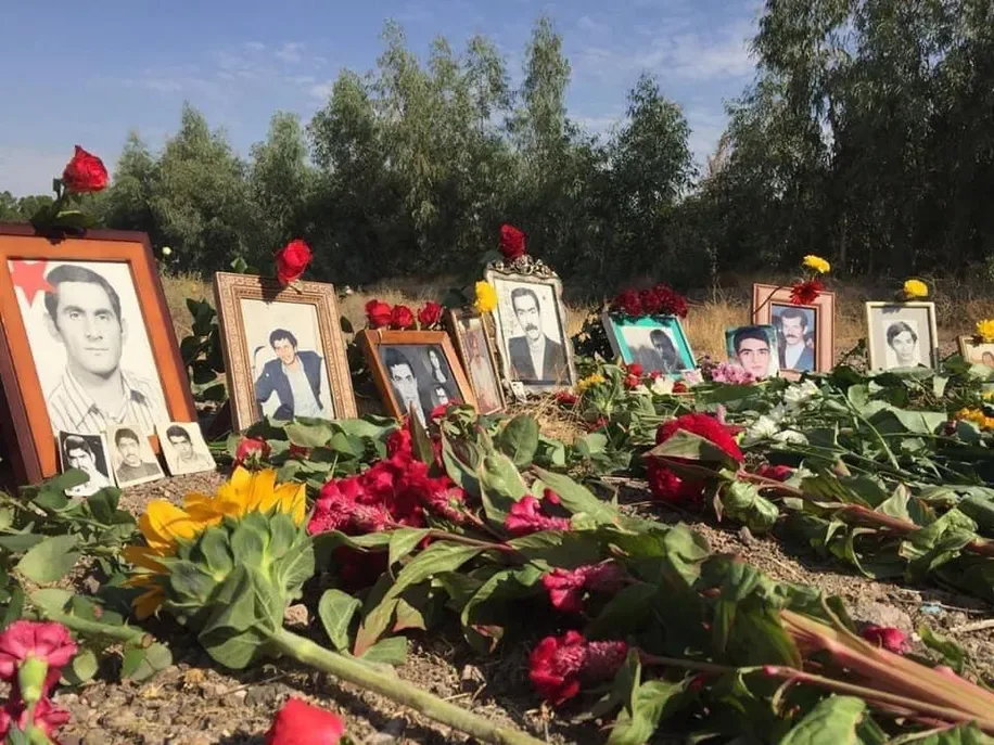 Black-and-white portraits of executed prisoners in frames, propped among red and yellow flowers on the ground at Khavaran.